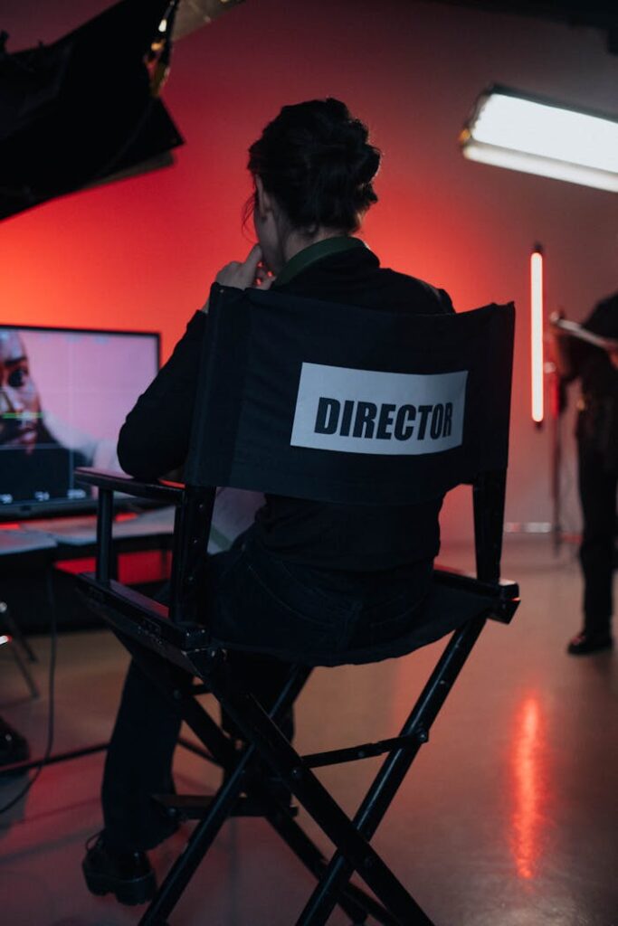 Director sits on chair in moody film studio, overseeing production setup.
